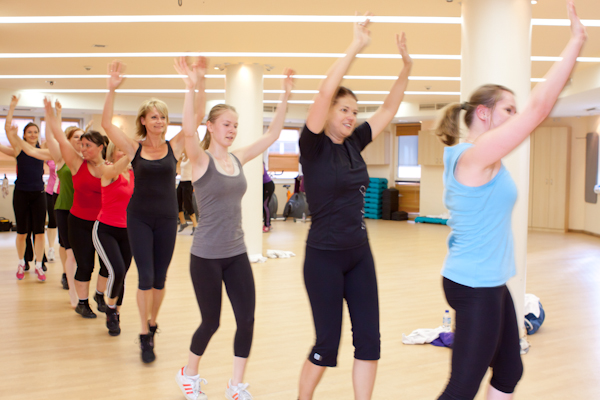 FitFusion csoportos óra: a csapat felemelt karral, egyszerre lép a zenére a tükrös teremben